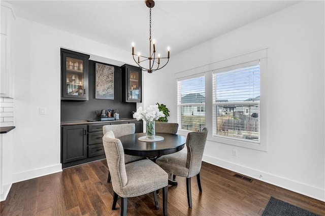 dining room with dark wood-style flooring, visible vents, baseboards, and an inviting chandelier