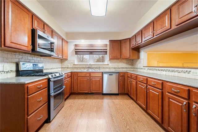 kitchen with tasteful backsplash, appliances with stainless steel finishes, sink, and light hardwood / wood-style floors