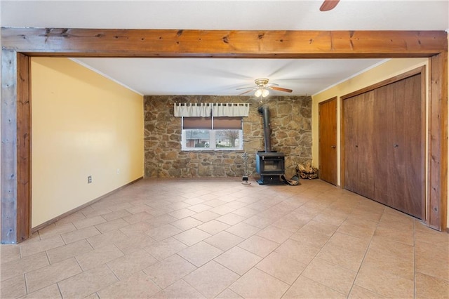 unfurnished living room featuring crown molding, ceiling fan, beam ceiling, and a wood stove