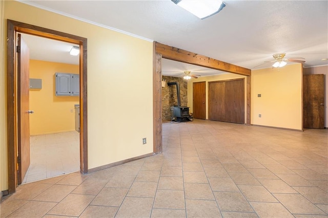 unfurnished room with light tile patterned flooring, ceiling fan, ornamental molding, and a wood stove