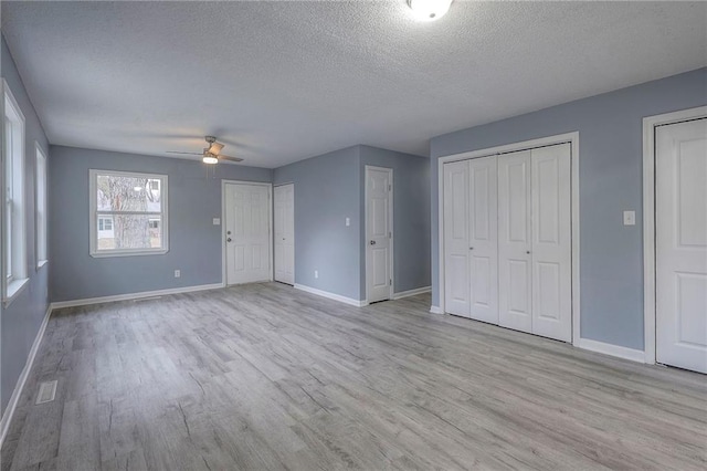 unfurnished bedroom featuring ceiling fan, two closets, light hardwood / wood-style flooring, and a textured ceiling