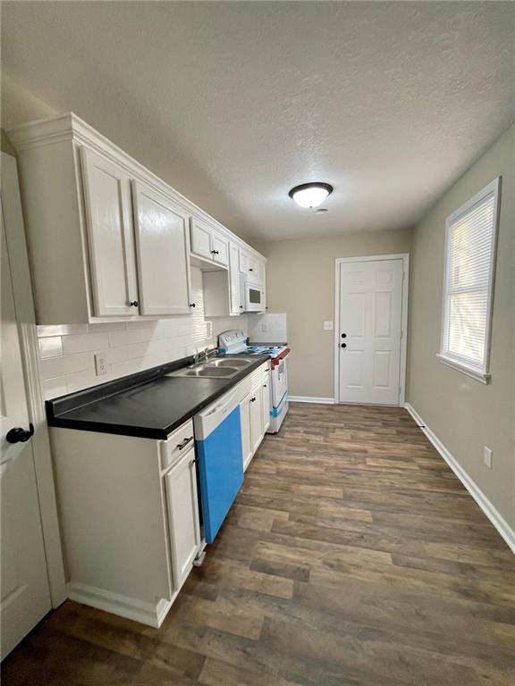 kitchen with dark wood-type flooring, white appliances, backsplash, and white cabinets