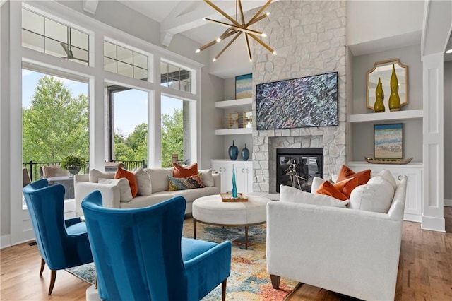 living room with a notable chandelier, high vaulted ceiling, built in features, wood finished floors, and a stone fireplace