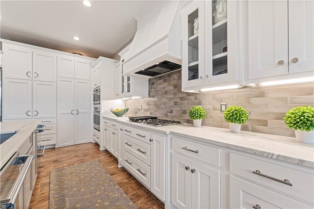 kitchen featuring white cabinetry, decorative backsplash, custom range hood, and light wood-type flooring