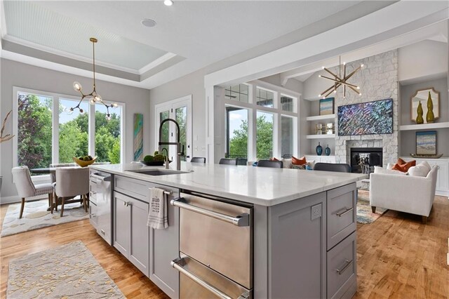 kitchen with light wood finished floors, gray cabinets, a sink, a raised ceiling, and a notable chandelier