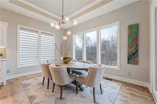 dining area with a tray ceiling, baseboards, light wood finished floors, and a chandelier