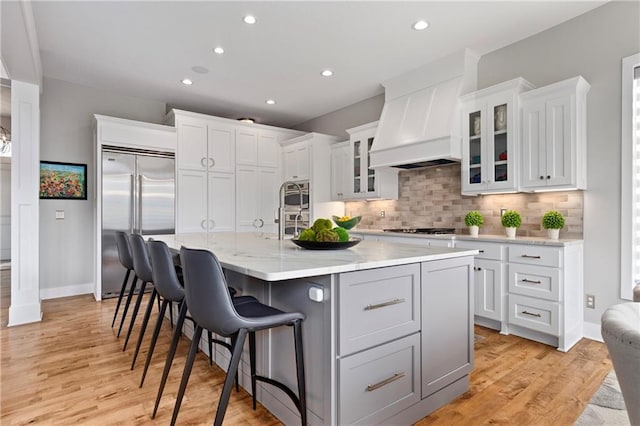 kitchen featuring tasteful backsplash, light wood-style floors, premium range hood, and stainless steel built in refrigerator