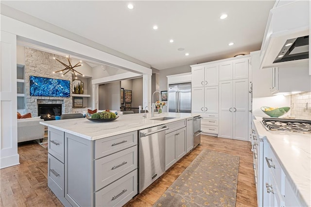 kitchen with a center island with sink, premium range hood, gray cabinets, a sink, and appliances with stainless steel finishes