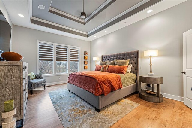 bedroom with baseboards, a raised ceiling, wood finished floors, and ornamental molding