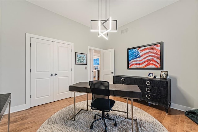 office space with an inviting chandelier, visible vents, baseboards, and light wood finished floors