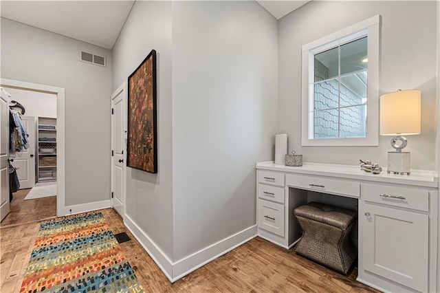 interior space featuring visible vents, baseboards, built in desk, and light wood finished floors