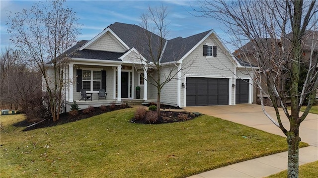 view of front facade with a front lawn, roof with shingles, covered porch, a garage, and driveway