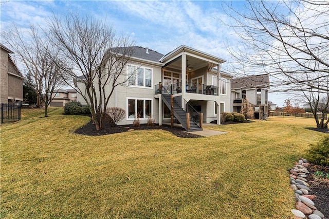 rear view of house with stairs, a lawn, fence, and stucco siding