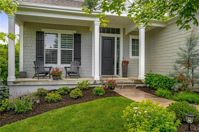 entrance to property featuring covered porch and roof with shingles