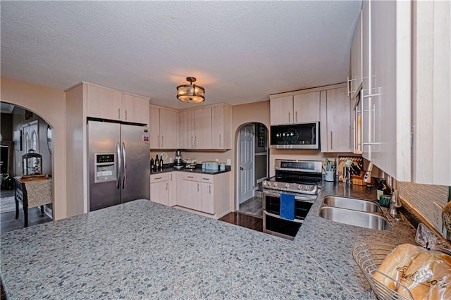 kitchen featuring sink, a textured ceiling, appliances with stainless steel finishes, kitchen peninsula, and dark stone counters