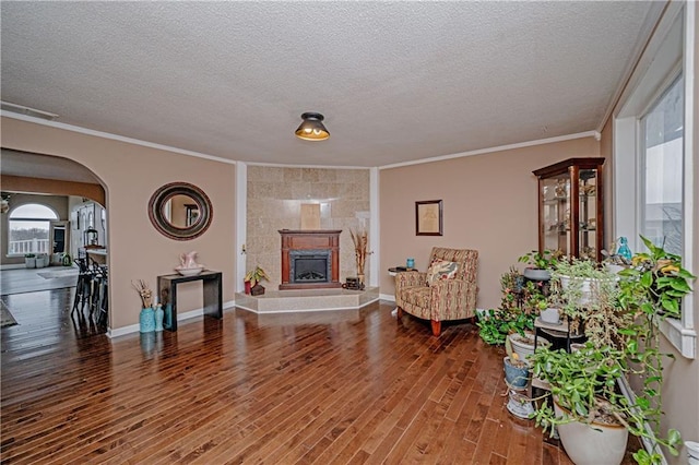 living room with hardwood / wood-style flooring, a tiled fireplace, ornamental molding, and a textured ceiling