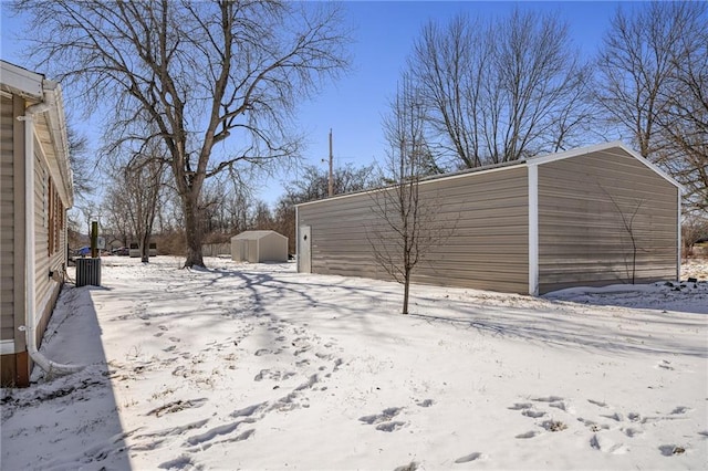 snowy yard with an outbuilding, a storage shed, and a detached garage