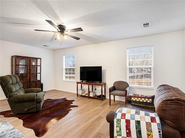 living room featuring ceiling fan, light hardwood / wood-style flooring, and a textured ceiling