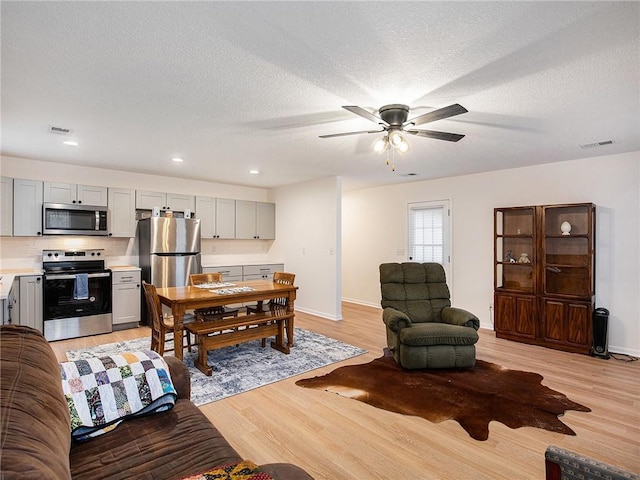 living room featuring ceiling fan, light hardwood / wood-style floors, and a textured ceiling