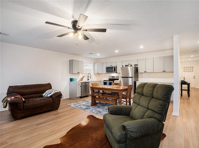 living room with sink, light hardwood / wood-style flooring, a textured ceiling, and ceiling fan