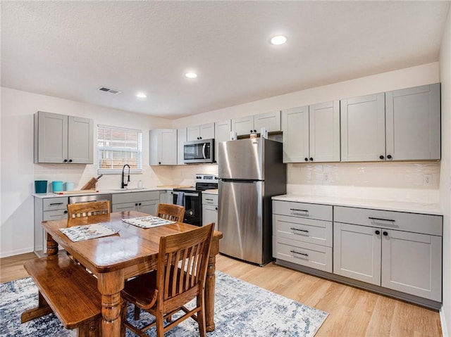 kitchen with stainless steel appliances, sink, light hardwood / wood-style floors, and gray cabinetry