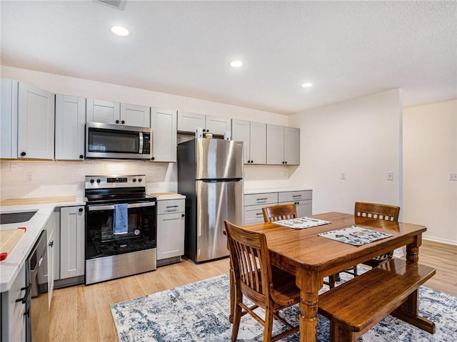 kitchen with decorative backsplash, stainless steel appliances, gray cabinets, and light hardwood / wood-style flooring