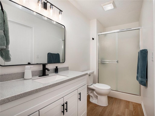 bathroom with vanity, hardwood / wood-style floors, a shower with shower door, and toilet