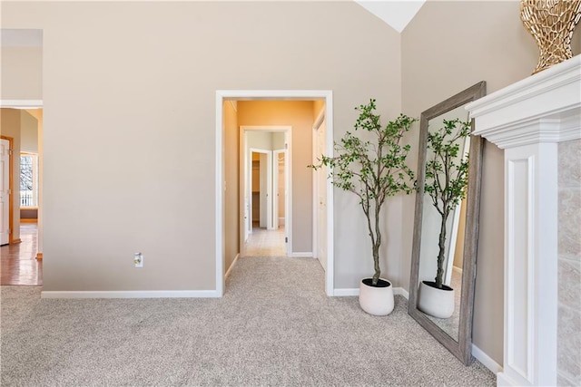 hallway with high vaulted ceiling, carpet flooring, and baseboards