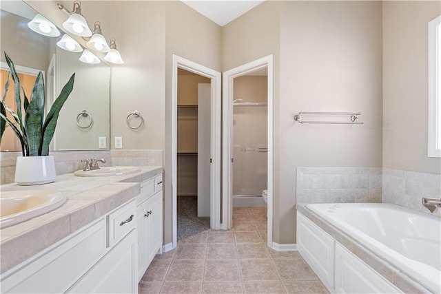 bathroom featuring a garden tub, a sink, tile patterned floors, double vanity, and a walk in closet