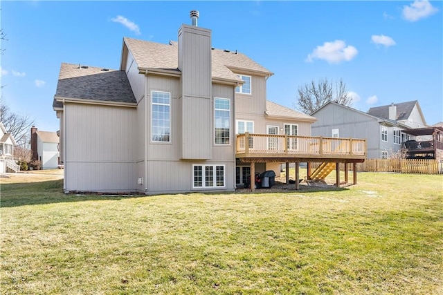 rear view of property with fence, roof with shingles, a lawn, a wooden deck, and a chimney