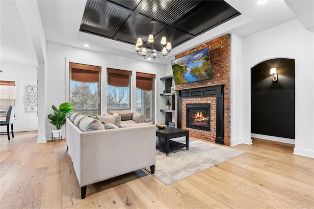 living room featuring a chandelier, light wood-type flooring, a fireplace, and baseboards