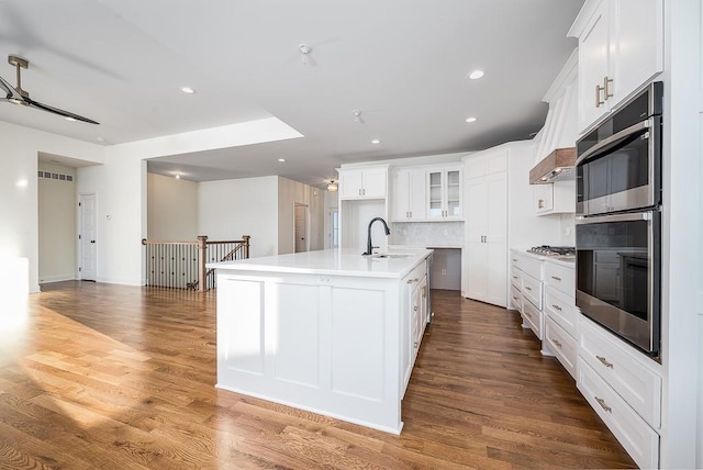 kitchen featuring wood-type flooring, sink, white cabinets, backsplash, and a center island with sink