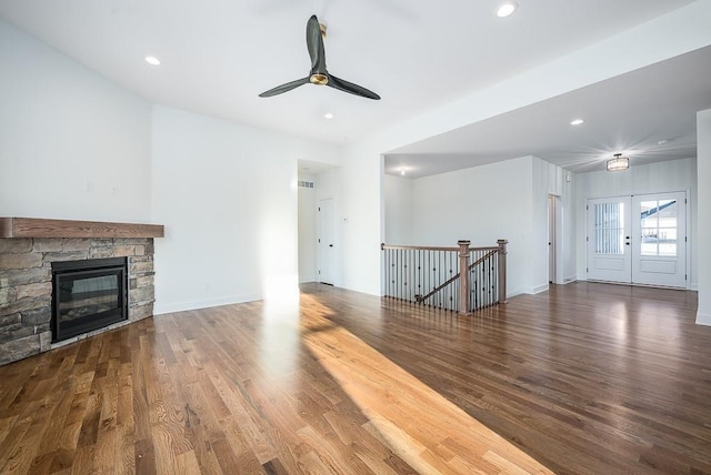 unfurnished living room featuring a stone fireplace, dark wood-type flooring, ceiling fan, and french doors