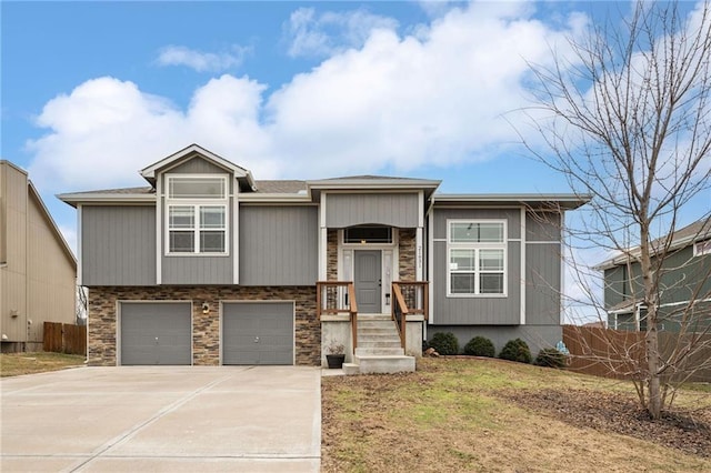 raised ranch featuring a garage, stone siding, fence, and concrete driveway