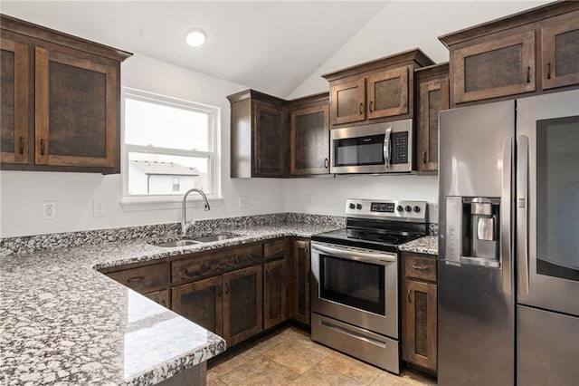 kitchen featuring lofted ceiling, appliances with stainless steel finishes, a sink, dark brown cabinets, and light stone countertops