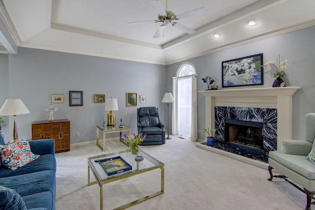 carpeted living room with ceiling fan, ornamental molding, a premium fireplace, and a raised ceiling