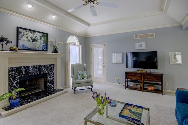 living room featuring a high end fireplace, ceiling fan, a tray ceiling, ornamental molding, and carpet