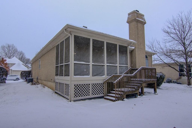 snow covered rear of property featuring a sunroom