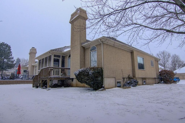 snow covered back of property featuring a sunroom