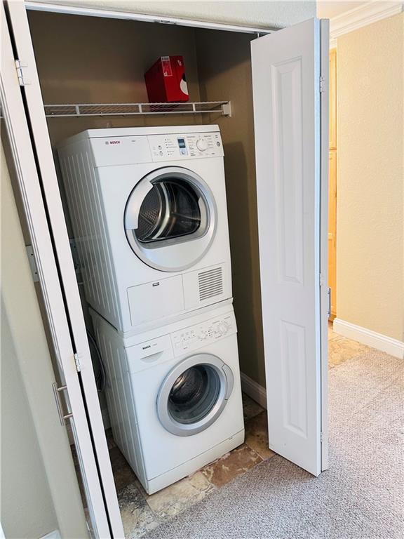 laundry room with stacked washer / drying machine and light colored carpet