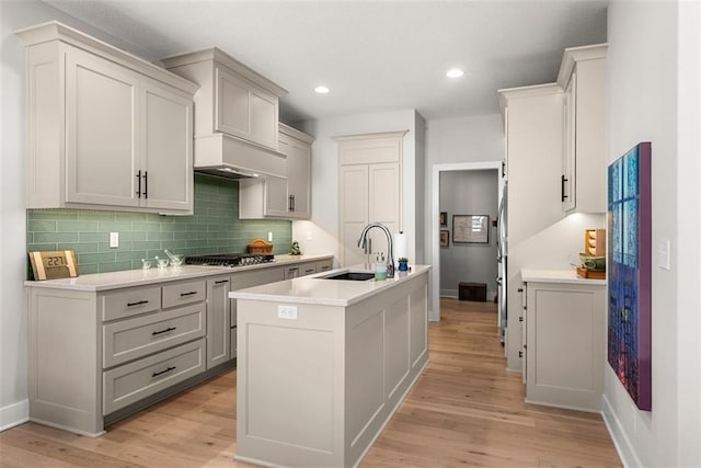 7209 Allman Dr, Shawnee, KS 66217 - kitchen featuring a sink, an island with sink, light wood-style floors, backsplash, and stainless steel gas stovetop