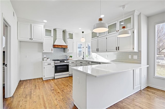 kitchen with glass insert cabinets, light countertops, premium range hood, and white cabinetry