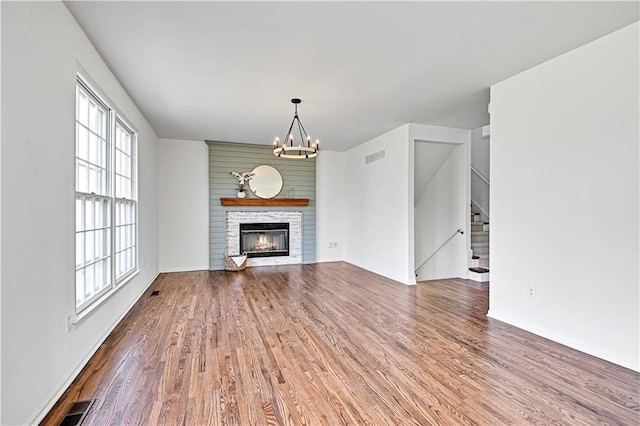 unfurnished living room featuring visible vents, an inviting chandelier, a glass covered fireplace, wood finished floors, and stairs