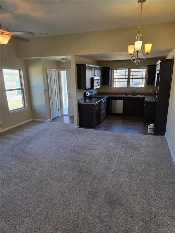 kitchen featuring decorative light fixtures, dark colored carpet, appliances with stainless steel finishes, open floor plan, and a sink