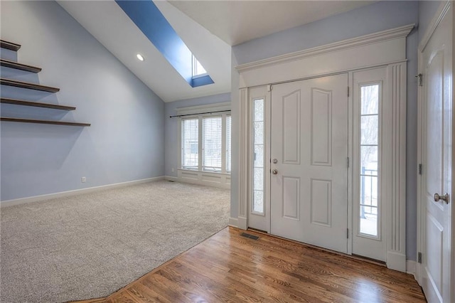 entryway with carpet floors, wood finished floors, visible vents, baseboards, and lofted ceiling with skylight