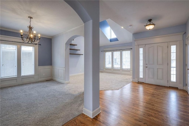 carpeted entrance foyer featuring arched walkways, ornamental molding, wood finished floors, a chandelier, and a decorative wall