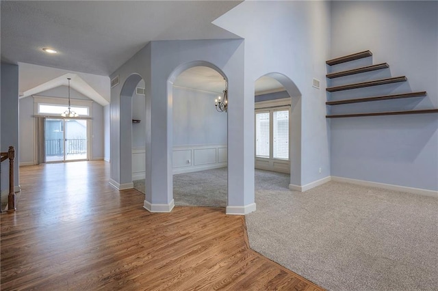 interior space featuring a chandelier, arched walkways, carpet floors, wood finished floors, and baseboards