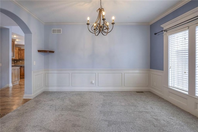 carpeted empty room with arched walkways, a decorative wall, visible vents, and crown molding