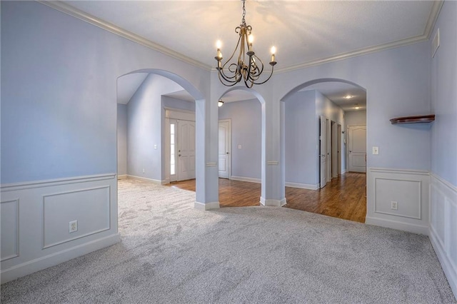 carpeted empty room featuring ornamental molding, arched walkways, a wainscoted wall, and a decorative wall