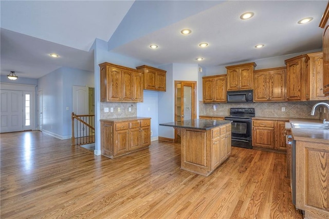 kitchen featuring brown cabinets, a kitchen island, a sink, light wood-type flooring, and black appliances